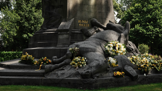 Foto van de sokkel van het Groeningemonument, close-up op het gevallen paard, omringd door bloemenkransen.