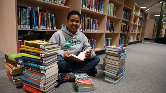 jongen in de bib tussen een stapel boeken