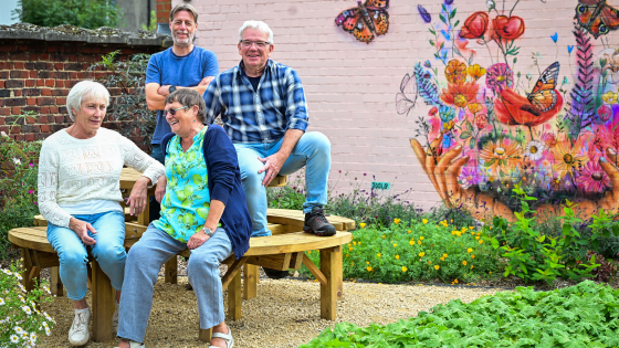 4 trotse buren poseren in de nieuwe vlindertuin met op de achtergrond een kleurrijke muurschildering